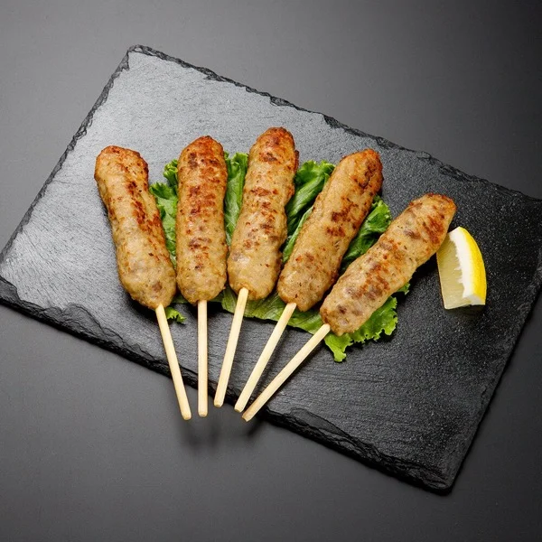 石板に並べた串刺しの牛たんつくね5本と、添えられたレモン