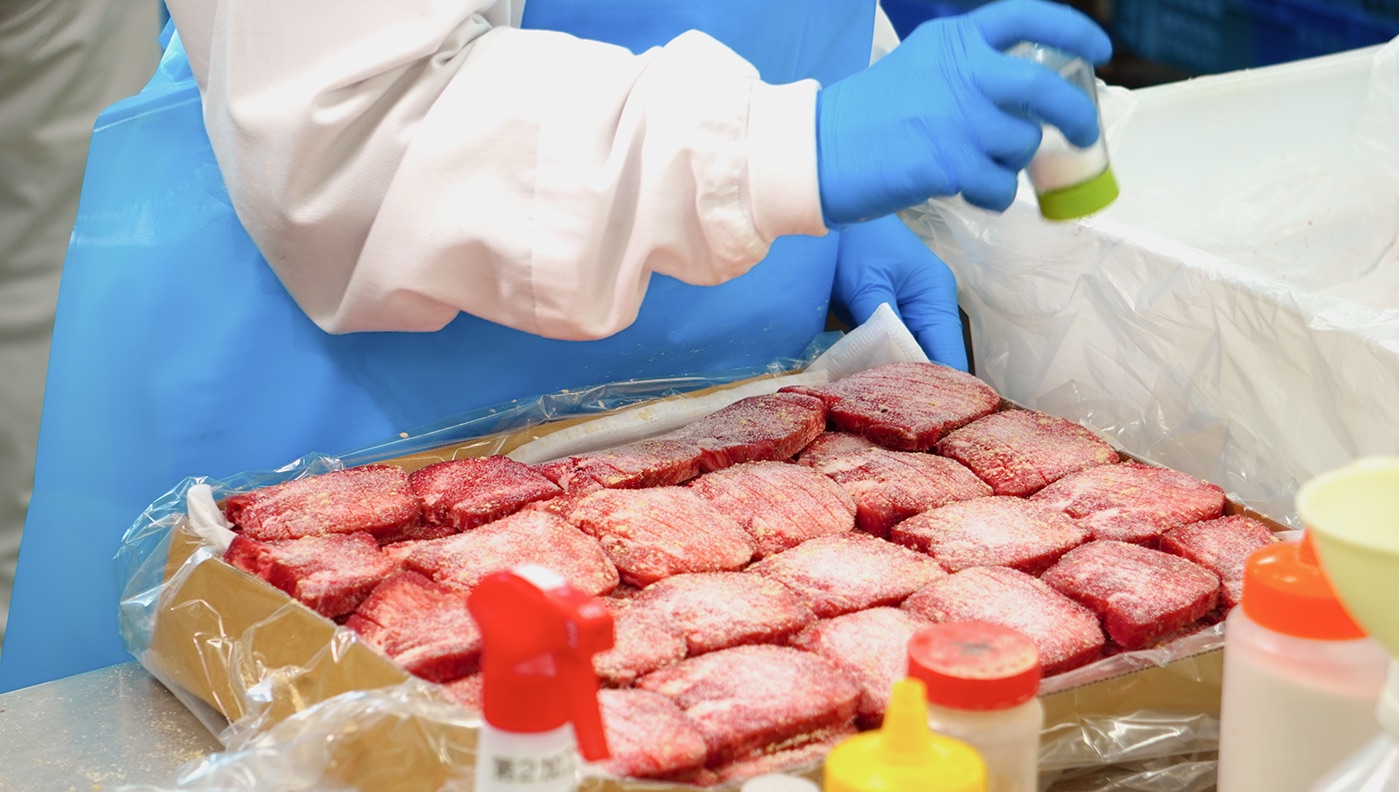 スライスした牛たんに、職人が手作業で味付けをしているところ
