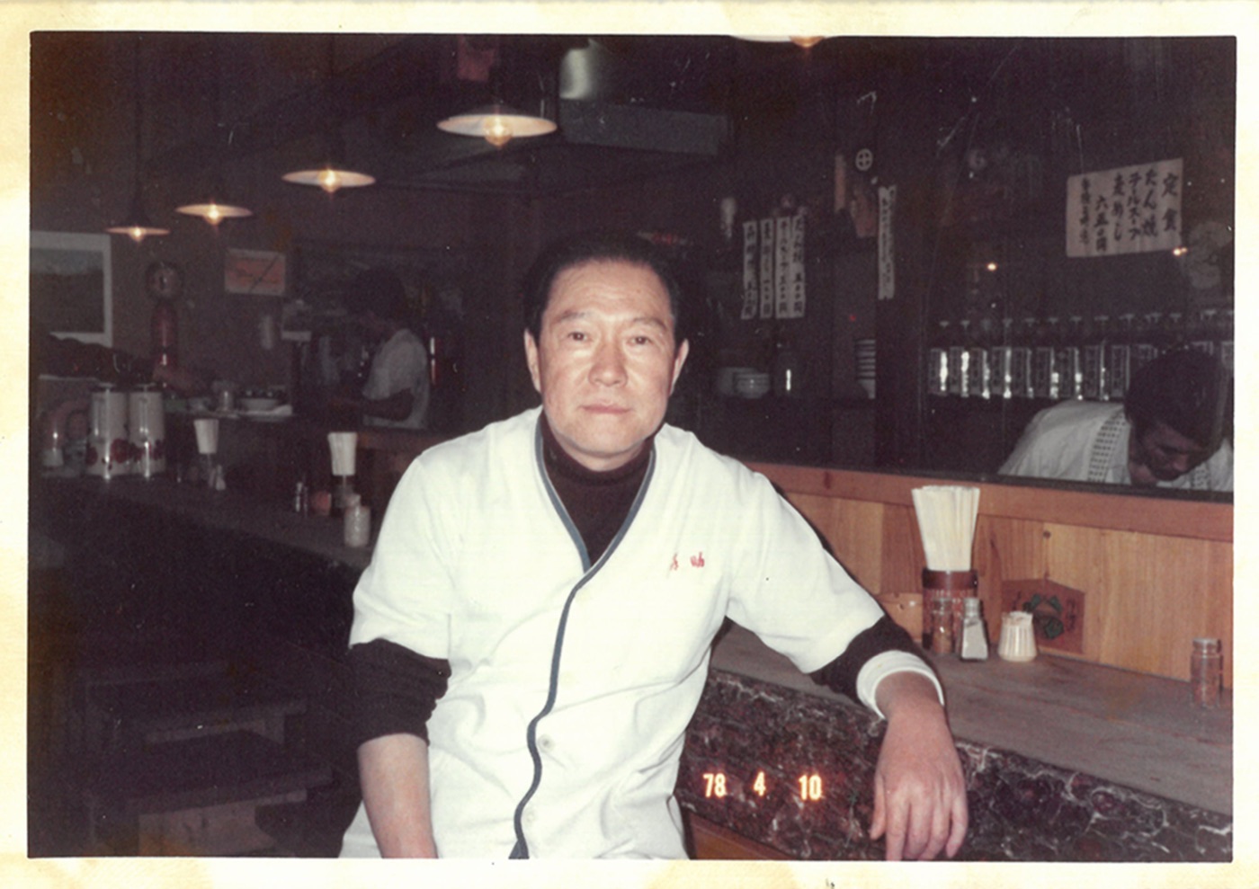1978年4月、一番町店のカウンター席に腰かける白い調理衣姿の喜助創業者・大川原要