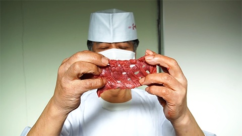 白衣の職人が、キッパの切れ込みで網の目のように開いた牛たんを両手で広げて確かめているところ