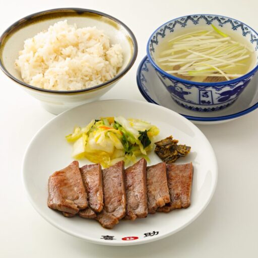 喜助の牛たん定食一式。喜助の銘が入った皿に牛たん焼きとお新香とみそ南蛮、麦飯の茶碗、白髪ねぎを浮かべた染付の碗のテールスープが並んでいる