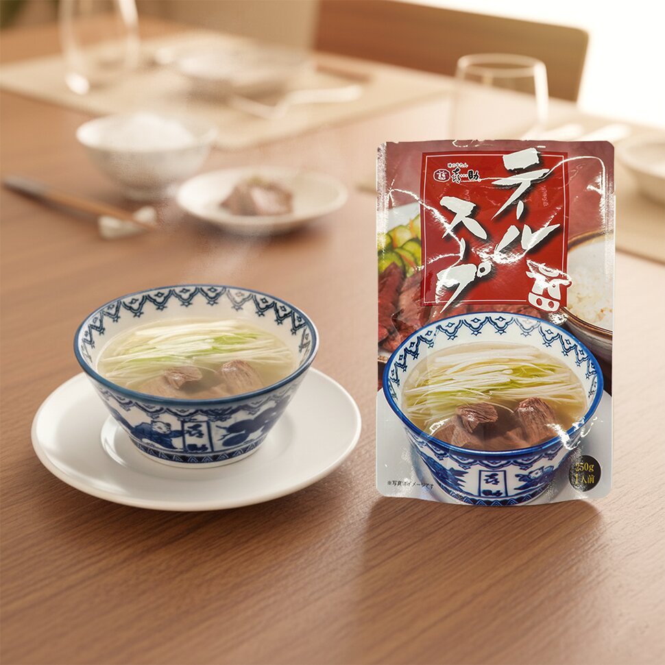 染付の碗に注いだテールスープ。白髪ねぎが浮かび、牛たんが入っている。隣にテールスープのパッケージが立ててある