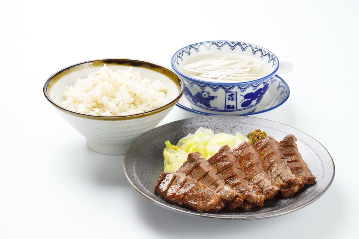 厚切りの牛たん焼きにお新香とみそなんばんを添えた皿、麦飯の丼、染付の器のテールスープを並べた特切り厚焼定食